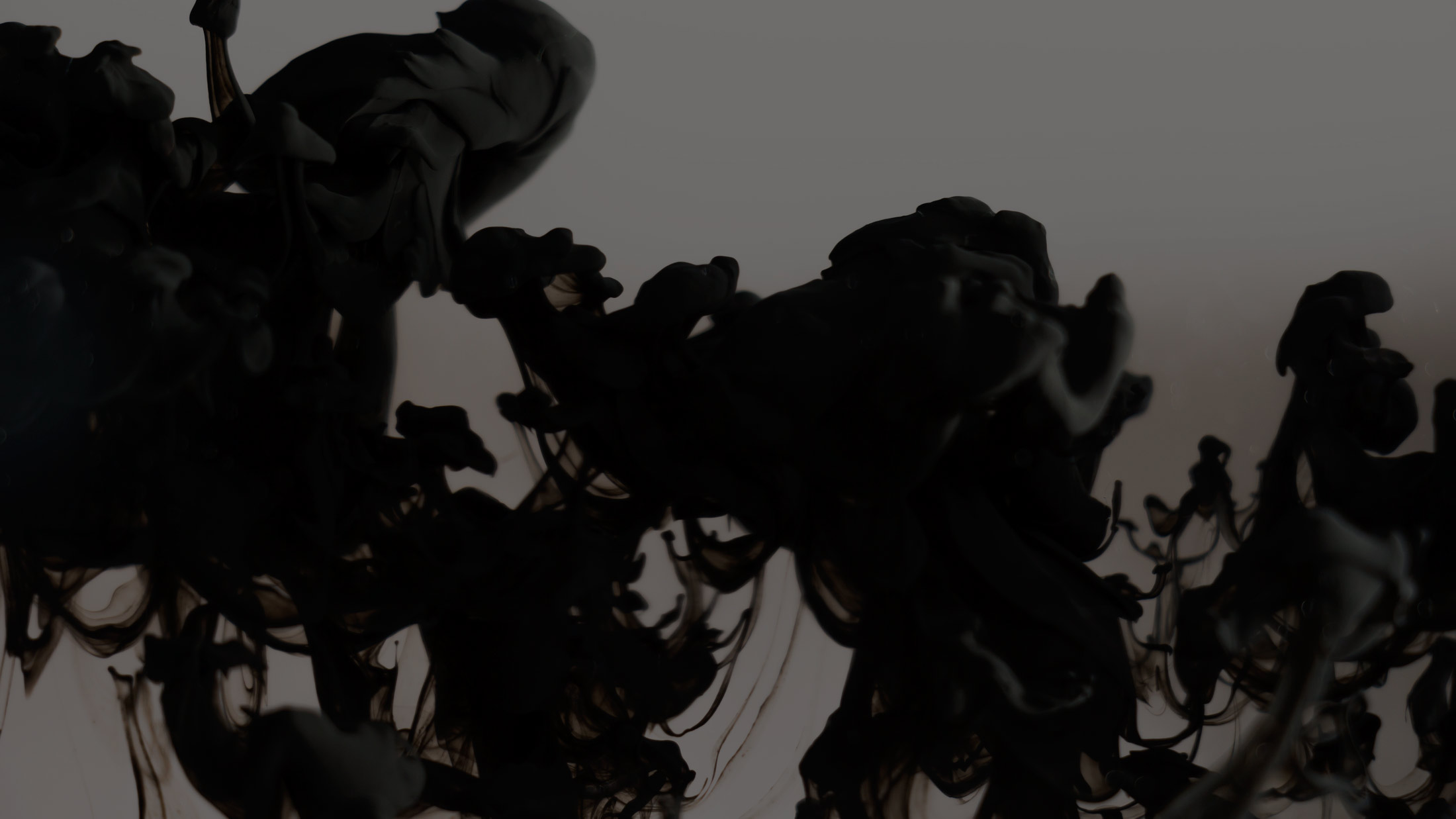 Dark abstract swirls of black ink and smoke drifting across a muted charcoal background, moody and atmospheric